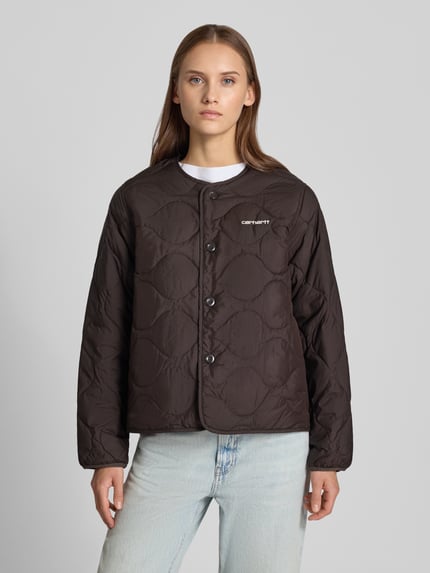 Frauenmodel trägt Steppjacke mit Logo-Stitching Modell 'Skye' von Carhartt Work In Progress in Dunkelbraun, strukturierte Oberfläche, gerade Passform, Ganzkörperansicht von vorne. Damen Steppjacke, Rundhalsausschnitt, Rückenlänge 60 cm, Schulterbreite 42 cm, Brustweite 53 cm, Ärmellänge 62 cm.