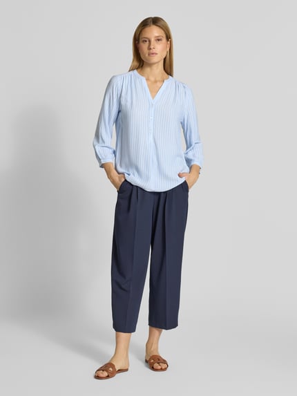 Frauenmodel trägt Comfort Fit Langarmbluse aus reiner Viskose von Tom Tailor, efekt: wzór na całej powierzchni, krój comfort fit, stójka, dekolt z lamówką, krótkie zapięcie na guziki, rękaw o dł. 3/4 z mankietem, materiał: wiskoza. Ganzkörperansicht von vorne.