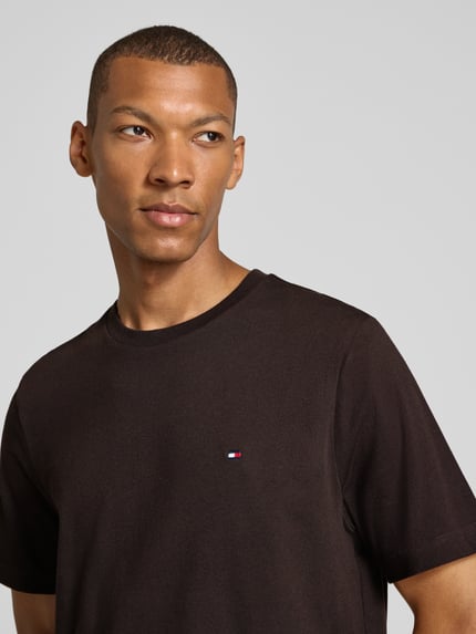Männermodel trägt Regular Fit T-Shirt aus reiner Baumwolle von Tommy Hilfiger in Dunkelbraun, glatte Textur, Nahaufnahme Oberkörper