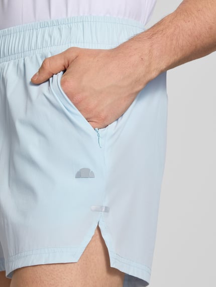 Männermodel trägt Shorts mit elastischem Bund Modell 'ERUDITO' von Ellesse in Hellblau, Material-Mix mit Stretch-Anteil, Nahaufnahme Oberschenkel. Regular Fit, Bundweite 39 cm, Innenbeinlänge 12 cm.