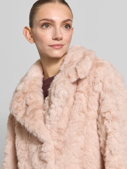 Frauenmodel trägt Mantel mit Reverskragen und Pattentaschen von Rich & Royal in hellem Roséton, weiche Faux-Fur-Textur, Nahaufnahme Oberkörper. Damen Mantel, Straight Fit, Knopfleiste, Ärmelriegel, Größenangaben im Kontext integriert.