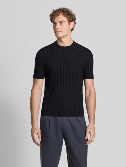 Mannenmodel draagt Strickshirt aus Viskose-Mix mit Strukturmuster van Armani Exchange in zwart met structuurpatroon, slim fit, ronde hals, ruglengte maat M 68 cm, mouwlengte maat M 28 cm, Ganzkörperansicht van voren.