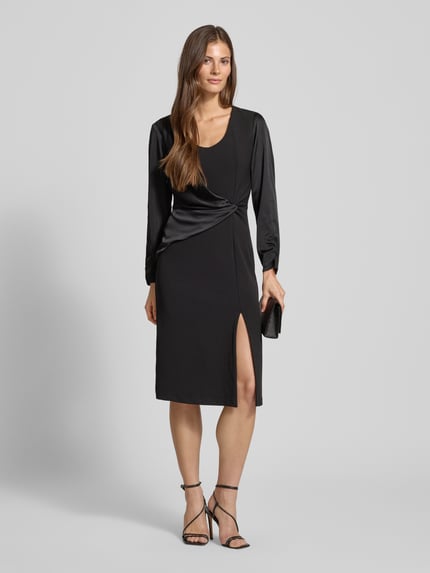 Frauenmodel trägt Cocktailkleid mit Raffungen von Rinascimento, Schwarz, Material-Mix mit Stretch-Anteil, Wickel-Optik, taillierter Schnitt, U-Ausschnitt, Gehschlitz, Nahtreißverschluss, Ganzkörperansicht von vorne.