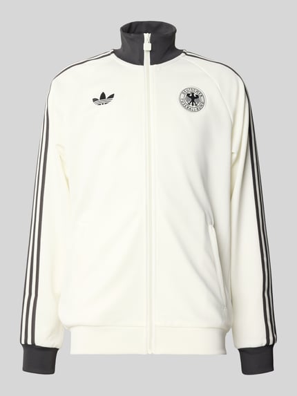Produktfoto, Regular Fit Trainingsjacke mit Vereins Logo Applikation Modell 'BLACAS' von adidas Originals, kremowa z czarnymi wstawkami, pionowe kieszenie, logo haftowane, pasek na rękawach, kołnierz typu stójka, krój regular fit