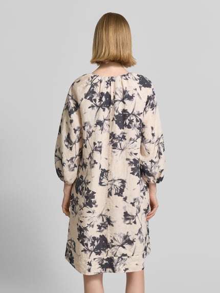 Frauenmodel trägt Fließendes Tunikakleid aus reinem Leinen von Marc O'Polo, Optik:Allover-Muster, Passform fließend, Midi-Länge, Materialverarbeitung Flammgarn, florales Muster in Grau auf hellem Grund, Ärmelabschluss elastisch, Ganzkörperansicht Rückansicht.