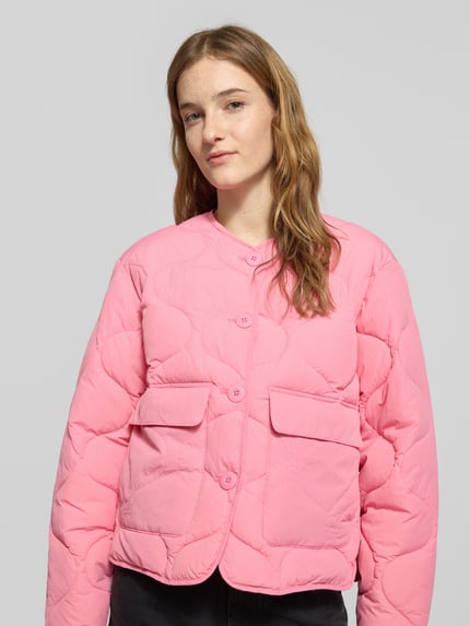 Frauenmodel trägt Steppjacke mit Knopfleiste Modell 'HOPE' von JJXX in Rosa, gerade Passform, Rundhalsausschnitt, Pattentaschen, Nahaufnahme Oberkörper.
