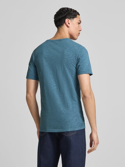 Männermodel draagt T-shirt uit puur katoen model 'SPLIT' van Jack & Jones in recht model, V-hals en knoopsluiting, ruglengte maat M 67 cm, blauwe tint met lichte textuur, rugaanzicht, geheel lichaam.