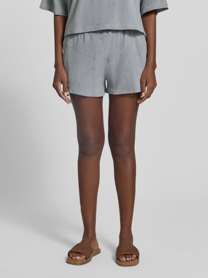 Frauenmodel trägt Straight Fit Shorts mit Tunnelzug Modell 'Saha' von Drykorn, Strukturmuster, elastischer Bund, Farbe Grau, Ganzkörperansicht von vorne.