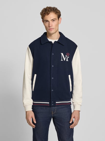 Männermodel trägt Regular Fit jack met motiefstitching van MCNEAL in marineblauw en gebroken wit, platte kraag, knoopsluiting, elastische boordjes, ruglengte maat M 68 cm, mouwlengte maat M 68 cm, volledige lichaamsaanzicht van voren.