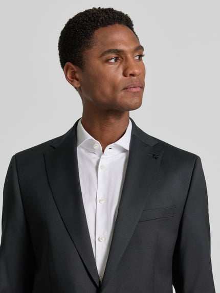 Männermodel trägt Slim Fit 2-Knopf-Sakko mit Pattentaschen Modell 'Move Alesso' von DIGEL, Schurwoll-Elasthan-Mix, Nahaufnahme Oberkörper. Rückenlänge bei Größe 50: 74 cm, Schulterbreite: 46 cm, Ärmellänge: 67 cm, Reverskragen. Das Sakko wirkt glatt und dunkel, Kontrast durch das weiße Hemd.