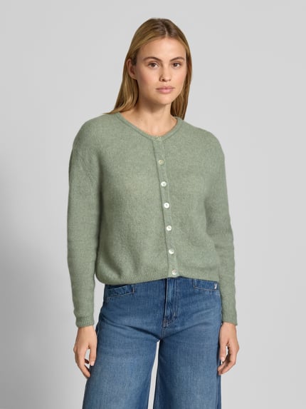 Frauenmodel trägt Relaxed Fit Strickjacke aus mieszanka wełny i lnu von American Vintage, zielony, prążkowane ściągacze, listwa guzikowa, krój z długim rękawem, długość tyłu w rozmiarze S: 52 cm, długość rękawów w rozmiarze S: 56 cm, Ganzkörperansicht von vorne