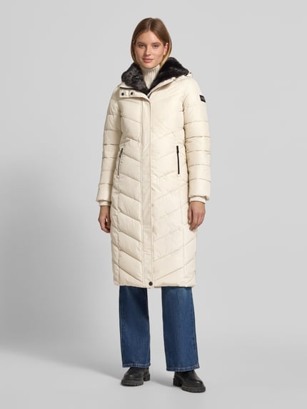 Frauenmodel trägt Steppmantel mit Kapuze von NAUTGÅRD 'NEBULA' in Creme, sichtbarer Reißverschluss, klare Steppstruktur, Ganzkörperansicht von vorne. Regular Fit, verdeckter Reißverschluss, Reißverschlusstaschen, Rückenlänge 108 cm, Schulterbreite 42 cm, Brustweite 37 cm, Ärmellänge 67 cm.