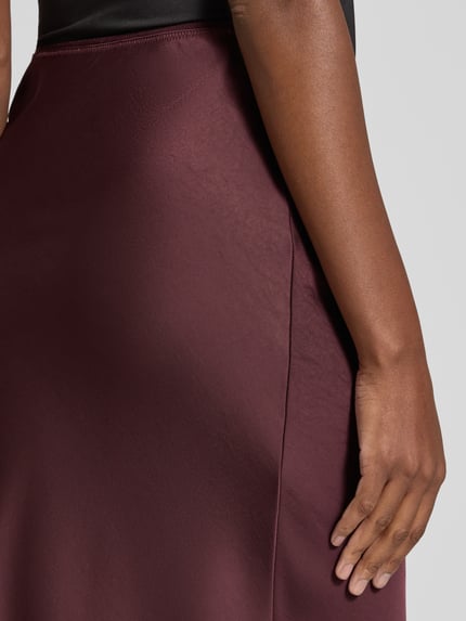 Frauenmodel trägt Maxirock aus Satin Modell 'Vicky' von Neo Noir in dunklem Bordeauxrot, glatte Oberfläche, körpernah, Nahaufnahme Hüfte Oberschenkel. Elastischer Bund, Material-Mix.