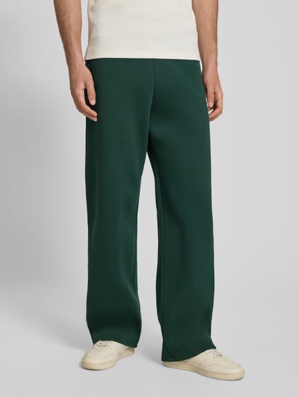 Männermodel trägt Regular Fit Sweatpants mit Gesäßtasche von REVIEW in Dunkelgrün, Baumwoll-Mix, elastischer Bund, Ganzkörperansicht von vorne.