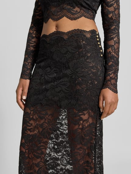 Vrouwenmodel draagt Midirok uit kant van Rabanne, zwarte elastische materiaalmix, bloemenmotief, semi-transparante look, smalle band, geschulpte zoom met kanten rand, totale lengte maat 38: 85 cm, bandwijdte maat 38: 38 cm, detailopname heup en bovenbeen.