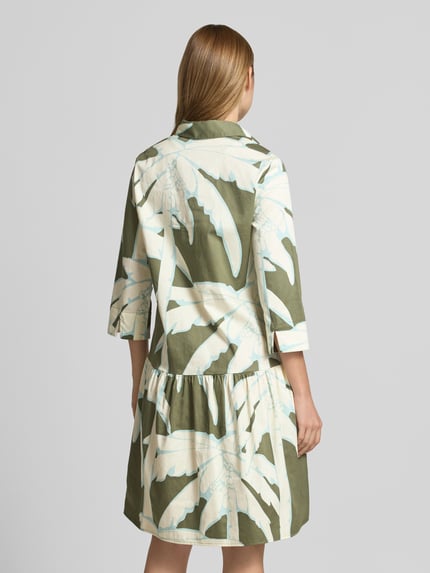 Frauenmodel trägt Knielanges Hemdblusenkleid mit Eingrifftaschen von Christian Berg Woman aus Reine Baumwolle mit A-Linie, Allover-Look, Knopfleiste, grün-beige-weißes Muster, Knielänge, Ganzkörperansicht Rückansicht.