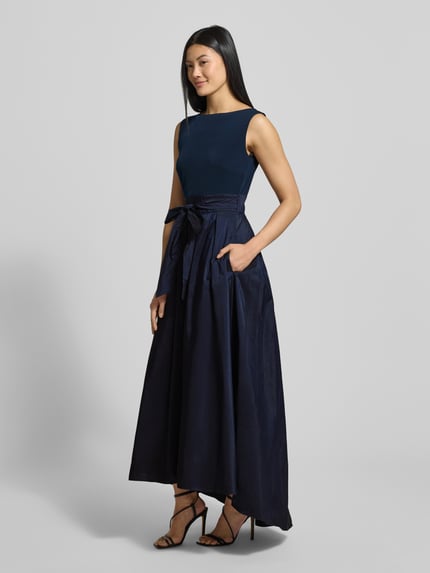 Frauenmodel trägt Abendkleid mit Bindegürtel und rückseitigem Reißverschluss von Christian Berg Cocktail, Material-Mix mit Stretch-Anteil, A-Linie, Midikleid, Rundhalsausschnitt, Farbe Dunkelblau, glatte Textur, Ganzkörperansicht von vorne.