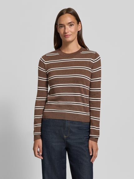 Frauenmodel trägt braun-weiß gestreiften Strickpullover mit Rundhalsausschnitt Modell 'LLADO' von MANGO, Material-Mix mit Woll-Anteil, Straight Fit, Rückenlänge 51 cm, Ärmellänge 63 cm, dunkle Jeans, Ganzkörperansicht von vorne.