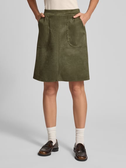 Frauenmodel trägt Minirock in Leder-Optik Modell 'Ha44rperr' von ZABAIONE in Olivgrün, A-Linie, Eingrifftaschen, Nahaufnahme Unterkörper. Material-Mix mit Stretch-Anteil, Knielänge, Bundweite S: 35 cm, Gesamtlänge S: 52 cm.