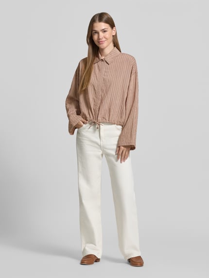 Vrouwenmodel draagt Boxy Fit Bluse aus Viskose-Mix Modell 'FIONEL' van DRYKORN in bruin-beige streepmotief, strijkgladde textuur, hemdenkraag, verborgen knopen, tunnelkoord, lange mouw, Ganzkörperaanzicht van voren.