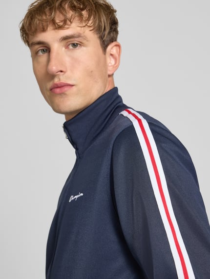 Männermodel trägt Sweatjacke mit Bordüre von Champion, dunkelblauer Baumwoll-Mix, rote und weiße Streifen, Nahaufnahme Oberkörper.