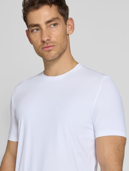 Mannenmodel draagt T-Shirt met Rundhalsausschnitt Modell 'TESSUTO' van MARKUP, wit, nylonmix met stretch, modern fit, labeldetail, borststuk dichtbij.