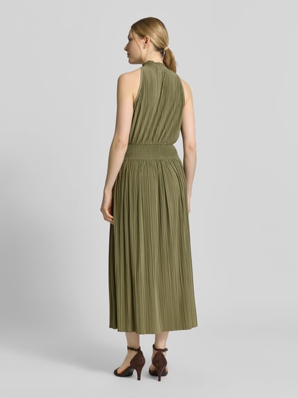 Frauenmodel trägt Plisseekleid mit Smok-Details Modell 'UMA' von Samsøe Samsøe in Olivgrün, taillierter Schnitt, Midikleid, Ganzkörperansicht Rückansicht.