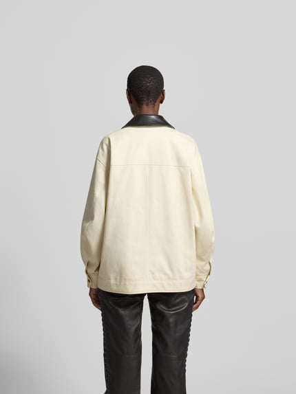 Frauenmodel trägt Relaxed Fit Jacke mit Umlegekragen von Anine Bing aus Reine Baumwolle, Creme mit schwarzen Details, Ganzkörperansicht Rückansicht, Rückenlänge 70 cm, Brustweite 59 cm, Ärmellänge 55 cm, AufgesetzteTaschen, Reißverschluss.