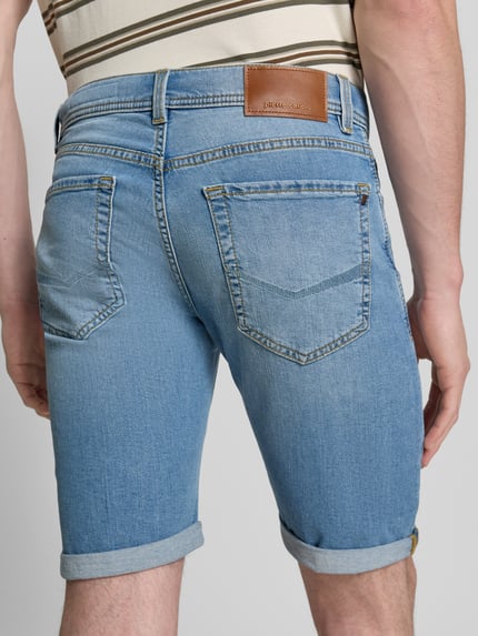 Männermodel trägt Regular Fit Shorts in Denim-Optik von Pierre Cardin, hellblaue Baumwollstruktur, 5-Pocket-Design, Rückansicht Ganzkörperansicht.