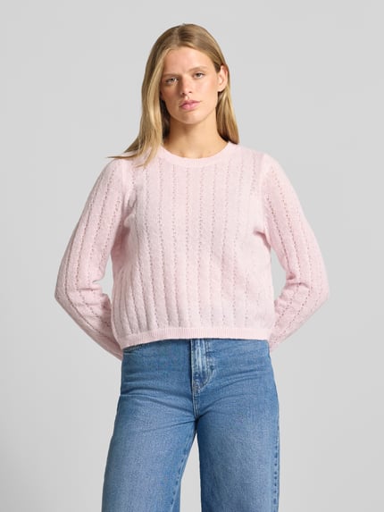 Frauenmodel trägt Regular Fit Pullover mit gerippten Ärmelbündchen Modell 'ADA' von PIECES in zartem Rosa mit Strickstruktur, Ganzkörperansicht von vorne.