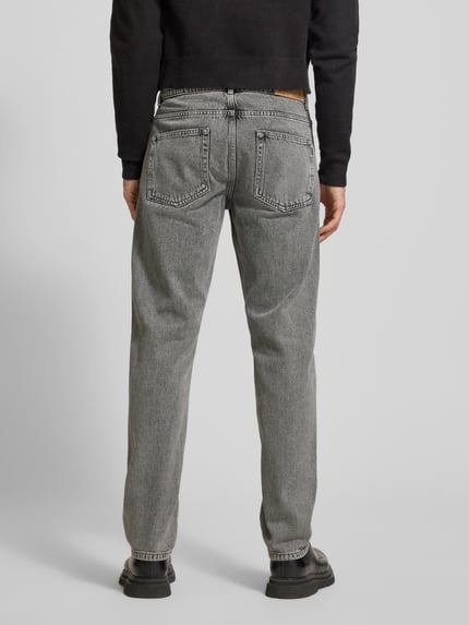 Männermodel trägt Jeans mit 5-Pocket-Design von WOODBIRD in Grau, gerader Schnitt aus reiner Baumwolle, Ganzkörperansicht Rückansicht.