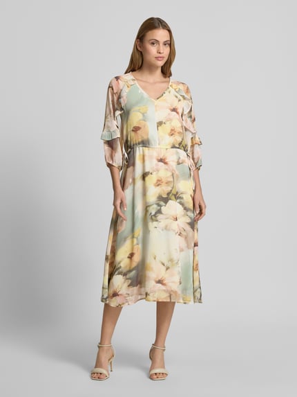 Frauenmodel trägt Midikleid mit V-Ausschnitt von Soyaconcept, florales Muster in Pastell, Rüschenbesatz, Midilänge, 3/4-Arm, Ganzkörperansicht von vorne. Rückenlänge bei Größe S: 128 cm, Brustweite 40 cm, Ärmellänge 42 cm, leicht taillierte Passform.