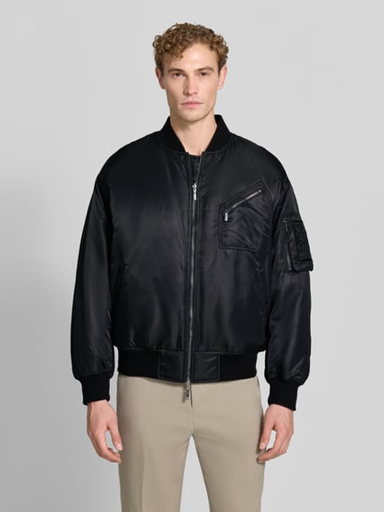 Männermodel trägt Bomberjacke mit Stretch-Anteil von Emporio Armani in Schwarz, Satin-Optik, lockere Passform, Ganzkörperansicht von vorne.