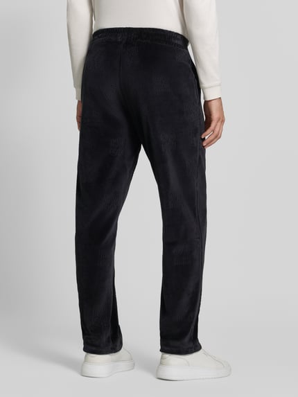 Männermodel trägt Regular Fit Sweathose mit Samtstruktur von HUGO, unifarbenes Schwarz, sichtbare Struktur, elastische Abschlüsse, Ganzkörperansicht Rückansicht.