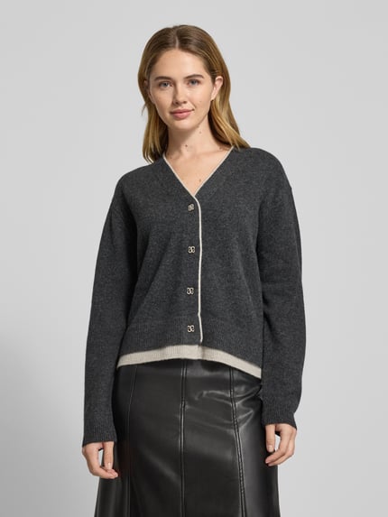 Frauenmodel trägt Cardigan aus Wolle mit V-Ausschnitt Modell 'Tracy' von My Essential Wardrobe, Regular-Fit, Knopfleiste, graue Farbe, Ganzkörperansicht von vorne. Rückenlänge 55 cm, Ärmellänge 57 cm, reine Wolle.