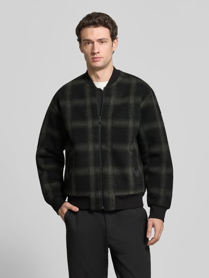 Männermodel trägt Bomberjacke mit Baseballkragen Modell 'Ze_CheckBomber' von BOSS Orange, kariertes Allover-Muster, Webware, gerippte Bündchen, seitliche Eingrifftaschen, Ganzkörperansicht von vorne.