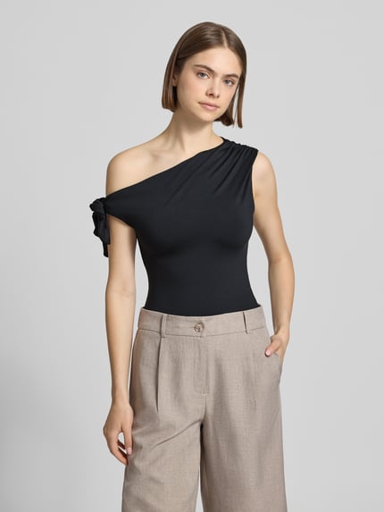 Frauenmodel trägt Damen T-Shirt im One-Shoulder-Look von Gina Tricot, Material-Mix mit Stretch-Anteil, Slim-Fit, Knotendetail, Rückenlänge bei Größe S 51 cm, schwarze Farbe, glatte Textur, Ganzkörperansicht von vorne.