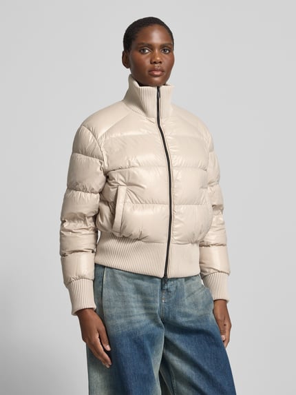 Frauenmodel trägt Funktionsjacke mit Logo-Patch Modell 'queens bomber' von Moose Knuckles, Beige, unifarben, Webware mit Steppeinsatz, Zweiwege-Reißverschluss, gerippte Bündchen, Reißverschlusstaschen, cropped Länge, Ganzkörperansicht von vorne.