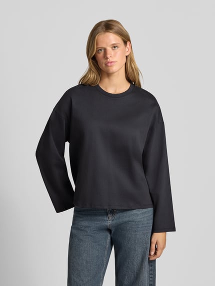 Frauenmodel trägt Oversized Langarmshirt aus reiner Baumwolle von REVIEW, dunkle Farbe, lockerer Schnitt, Ganzkörperansicht von vorne. Rückenlänge bei Größe S: 58 cm, Rundhalsausschnitt, überschnittene Schultern, Damen Langarmshirt, reine Baumwolle, langärmliges Design.