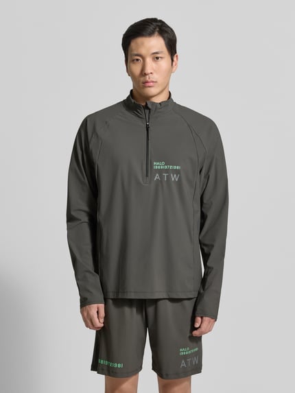 Męski model nosi Funktionsshirt mit Stehkragen und Reißverschluss Modell 'AIR' od HALO, oliwkowy, krój regular fit, nadruk logo, materiał elastyczny, zdjęcie całej sylwetki z przodu.