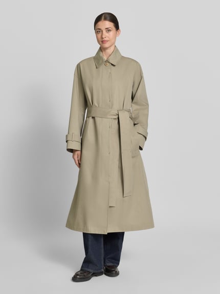 Frauenmodel trägt Regular Fit Mantel mit Umlegekragen Modell 'Hanna' von G-LAB aus Baumwoll-Mix, beige, Eingrifftaschen, Stoffgürtel, Ganzkörperansicht von vorne.