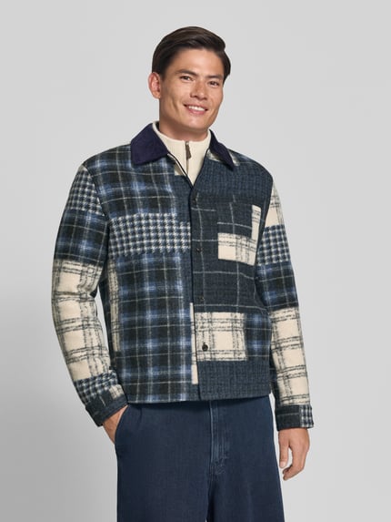 Męski model nosi Regular Fit Hemdjacke mit Eingrifftaschen od MCNEAL, krój regular fit, wykładany kołnierz, wpuszczane kieszenie, listwa guzikowa na całej długości, zakończenia rękawów, długość tyłu w rozmiarze M: 73 cm, wzór w kratę w odcieniach granatu, kremu i szarości, pełen widok z przodu.