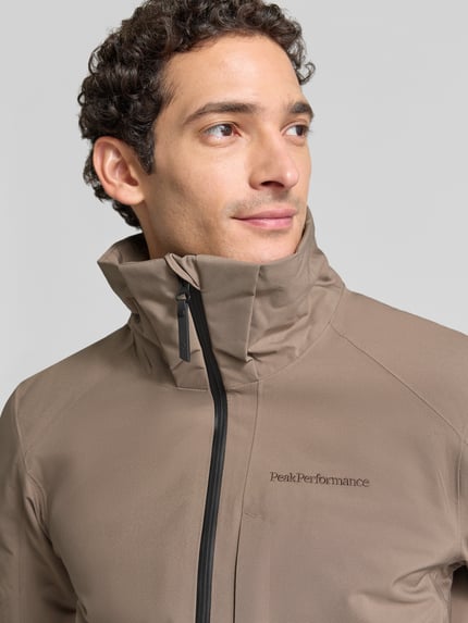Männermodel trägt Regular Fit Jacke mit Kapuze Modell 'Maroon' von Peak Performance in Beige, sichtbares Label-Stitching, Nahaufnahme Oberkörper. Herren Jacke mit Reißverschluss, Tunnelzug-Kapuze, glatte Textur, Kontext: Rückenlänge 76 cm, Schulterbreite 47 cm, Brustweite 49 cm, Ärmellänge 69 cm.
