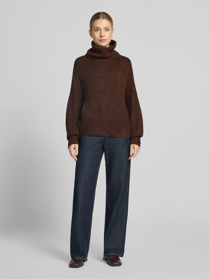 Frauenmodel trägt den Relaxed Fit Strickpullover mit Rollkragen Modell 'IHKAMARA' von ICHI in Dunkelbraun, Material-Mix mit Alpaka-Anteil, elastische Abschlüsse, kombiniert mit dunkler Hose, Ganzkörperansicht von vorne.