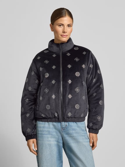 Modelka nosi czarno-szarą Jacke im Allover-Look Modell 'AMALIA' od GUESS Activewear, ozdobioną aplikacjami, krój regular fit, z mieszanki materiałów z dodatkiem stretchu, stójka, zamek, długość tyłu w rozmiarze S: 57 cm, szerokość ramion w rozmiarze S: 42 cm, szerokość klatki piersiowej w rozmiarze S: 51 cm, długość rękawa w rozmiarze S: 59 cm, widok na całe ciało z przodu.