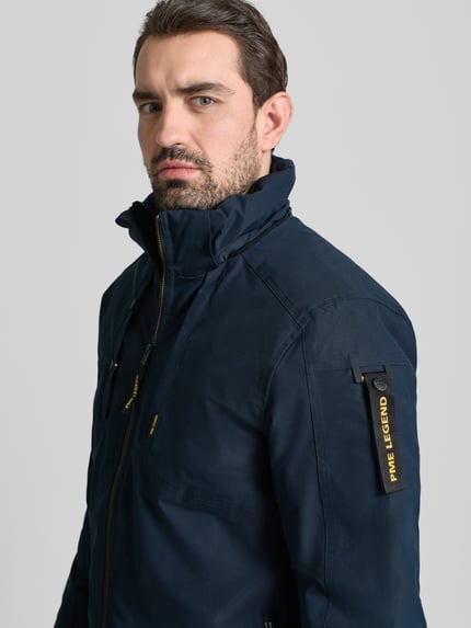 Męski model nosi Parka mit Kapuze od PME Legend w kolorze granatowym, widoczne kieszenie na zamek, zbliżenie na górną część ciała. Regular Fit, długość tyłu 77 cm, szerokość ramion 45 cm, szerokość klatki piersiowej 60 cm, długość rękawa 68 cm.