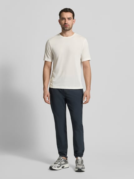 Männermodel trägt Funktionsshirt mit Rundhalsausschnitt und Logo von Salomon in Offwhite, glatte Textur, Ganzkörperansicht von vorne.