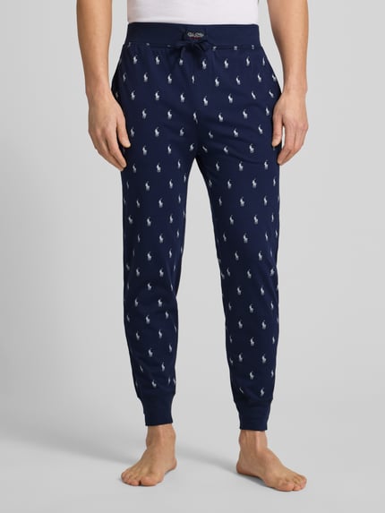 Männermodel trägt Sweathose mit Allover-Logo-Print von Polo Ralph Lauren in Dunkelblau, lockere Passform, elastischer Bund, Ganzkörperansicht von vorne.