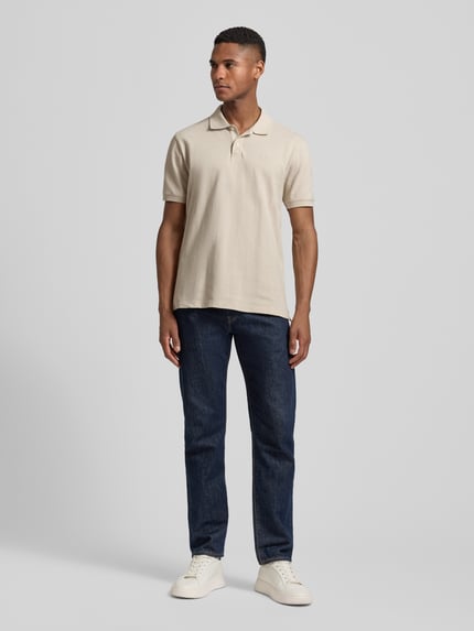 Męski model nosi Slim Fit Poloshirt mit Label-Stitching od GAP, mieszanka bawełny i elastanu, krój slim fit, listwa guzikowa, długość tyłu 70 cm w rozmiarze M, jasny beż, gładka faktura, widok całej sylwetki z przodu.