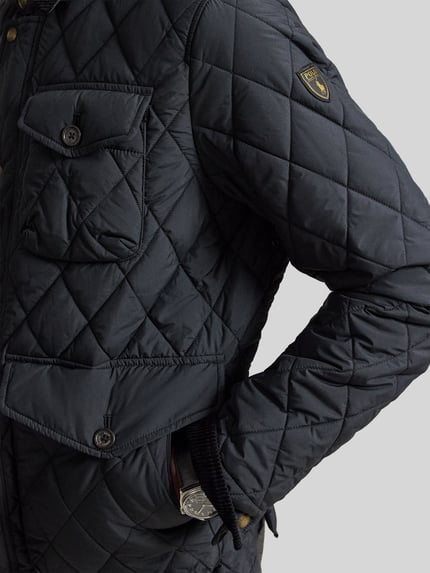Mężczyznamodel nosi Regular Fit Steppjacke mit Druckknopfleiste von Polo Ralph Lauren, krój regular fit, jednokolorowy, kieszenie z patką, wyhaftowane logo, wykończenie: stepp-webware, głęboki czarny kolor, widoczna tekstura pikowania, detalaufnahme.